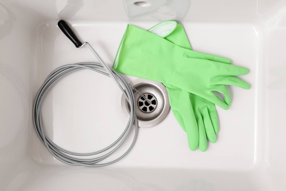 Sink with clogged drain, plumber's snake and rubber gloves, top view 